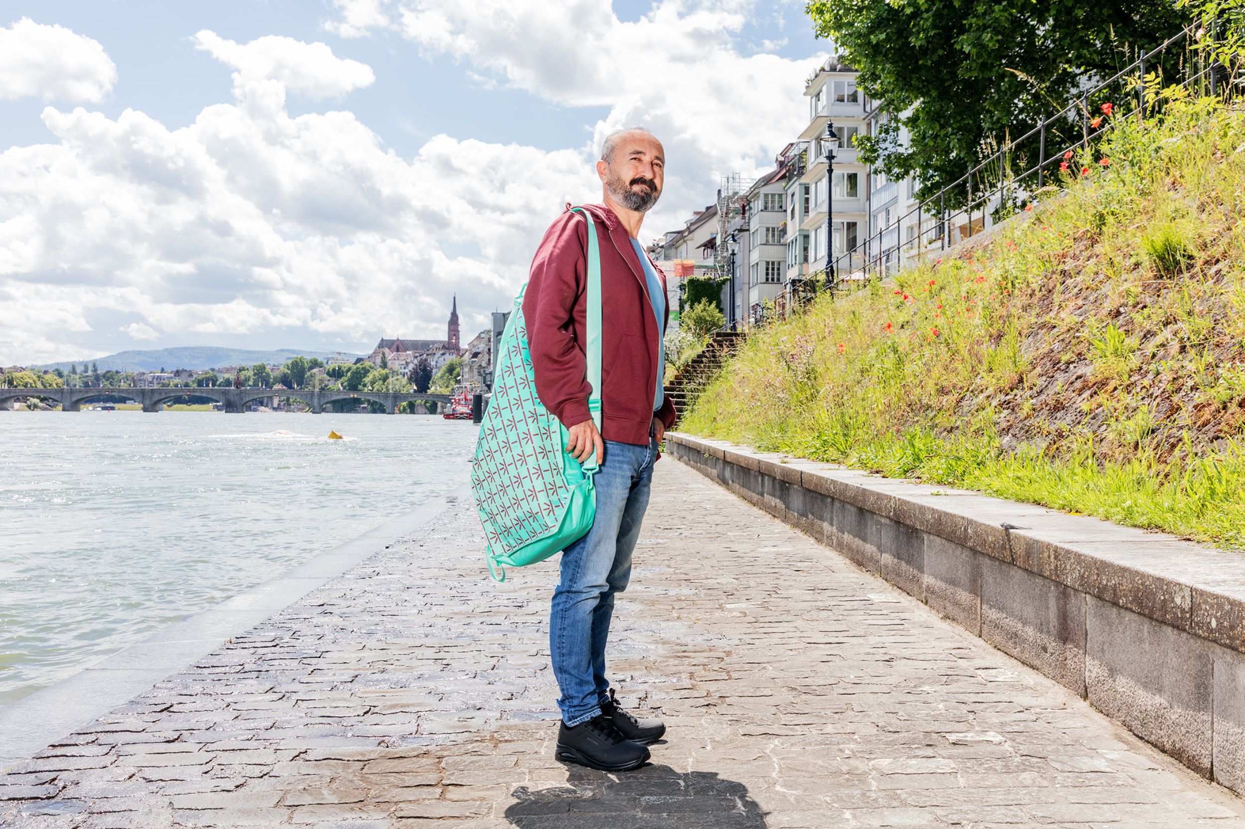 Employee with wine-red USB merchandise hoodie and turquoise swimming bag on the banks of the Rhine