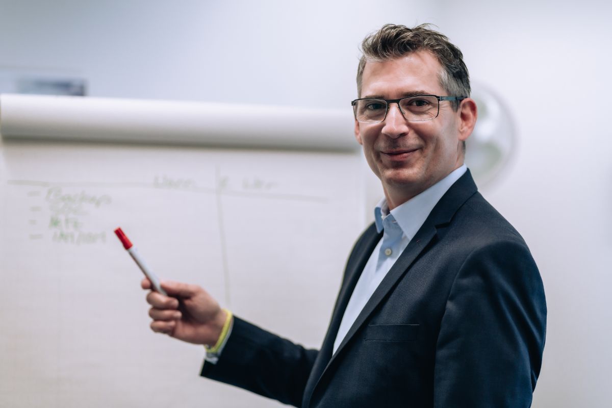 Man with glasses and suit points to a flipchart with a pen